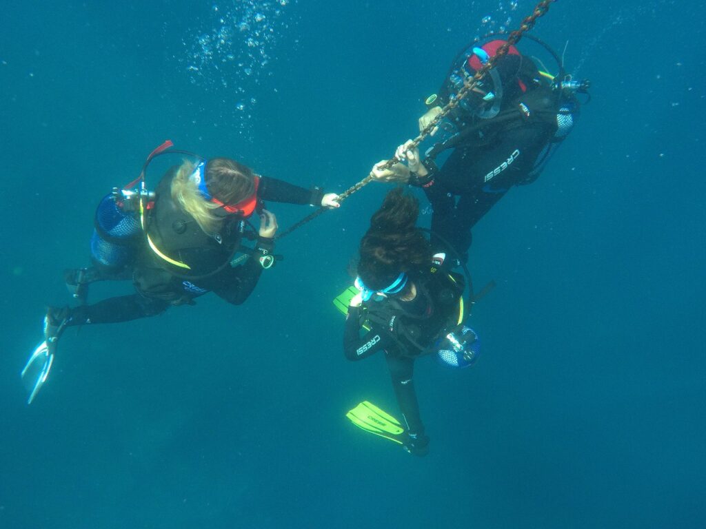 Tres buceadoras agarradas a una cadena bajo superficie